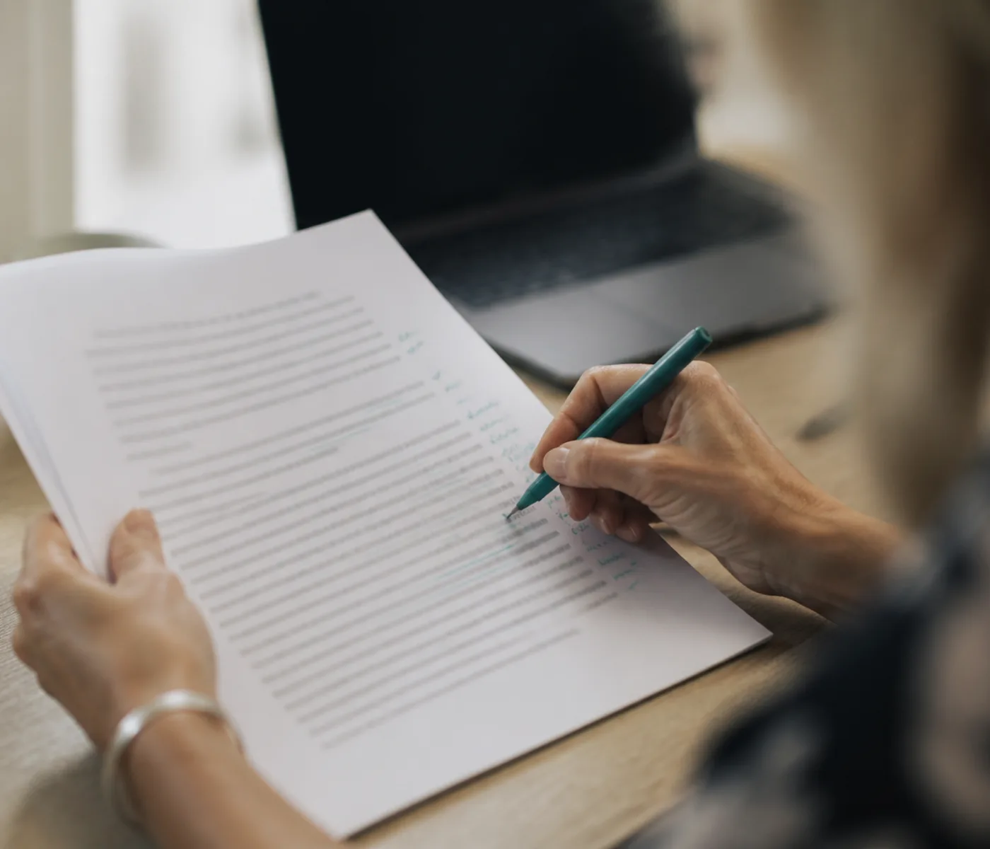 A qualified teacher annotating an IELTS writing answer by hand with a teal pen