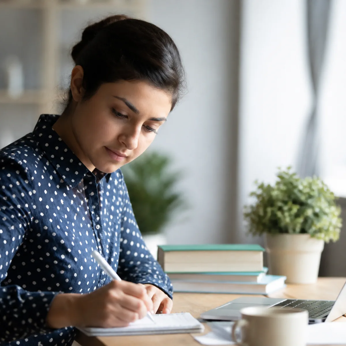 An international student writing an IELTS practice essay at a home desk